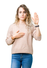 Beautiful young blonde woman wearing sweatershirt over isolated background Swearing with hand on...