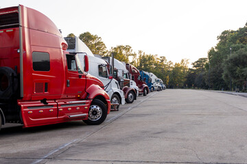 Row of colorful semi trucks lined up at dusk in a truck stop parking area.