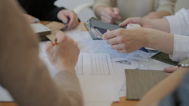A collaborative design meeting in action, with team members selecting materials and colors, consulting floor plans, and engaging in creative decision-making for an interior design project.