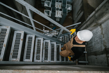 Top view of factory worker climbing metal stairs on industrial silo building..