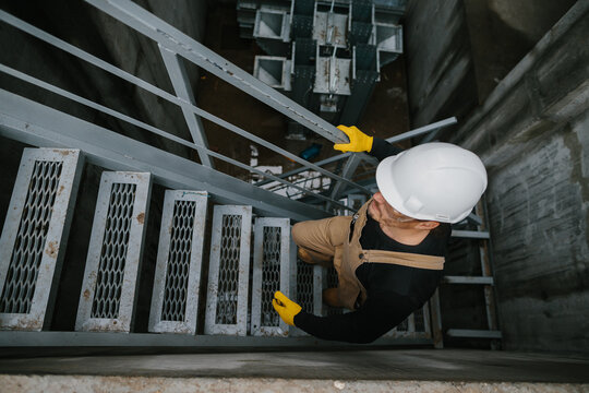 Top view of factory worker climbing metal stairs on industrial silo building..
