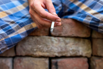 Man Sitting on Brick Wall with Cigarette in his Hands. Addiction and Bad Habits Concept.