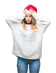 Beautiful young blonde woman wearing christmas hat over isolated background suffering from headache desperate and stressed because pain and migraine. Hands on head.