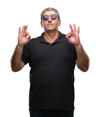 Handsome senior man wearing sunglasses over isolated background relax and smiling with eyes closed doing meditation gesture with fingers. Yoga concept.