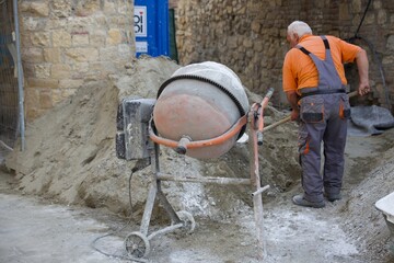 worker throws dry mixture into concrete mixer