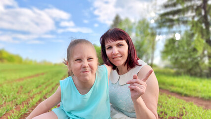 Fototapeta premium Happy mother and daughter enjoying rest, playing and fun on nature in green field. Woman and girl resting outdoors in summer and spring day