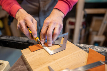Male hands cutting leather skin. Master measures right amount, uses construction knife, makes leather covers for the bed legs to prevent them from scratching floor.
