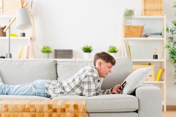Young man lying on the sofa using phone at home