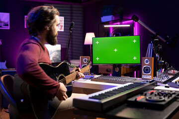 Artist learning to play guitar with internet lessons on greenscreen monitor, watching tutorials for acoustics rehearsal in home studio. Producer learns new string accords for music industry. - obrazy, fototapety, plakaty
