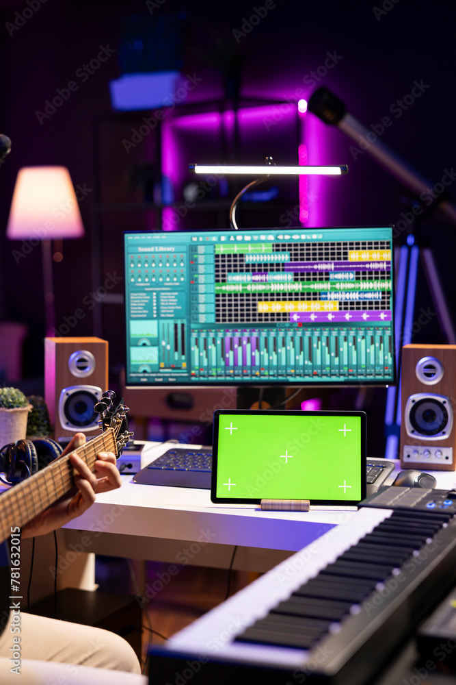 Leinwandbilder Audio producer practices playing guitar using learning tutorial on tablet via greenscreen display. Young artist learning to play acoustic instrument with online lessons, recording tunes.