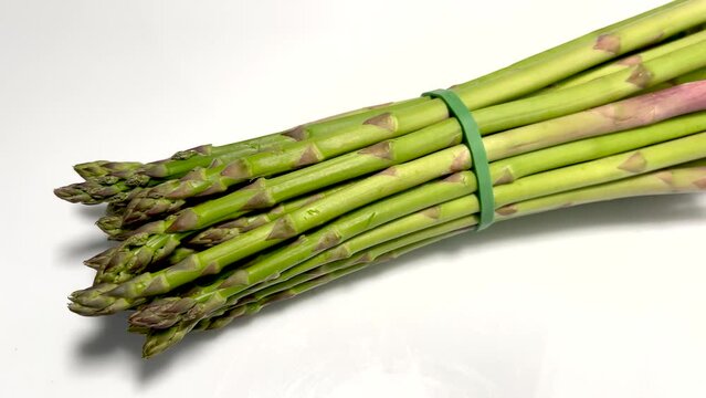 Tender freshly picked asparagus, zoom out on bunch of asparagus on white background