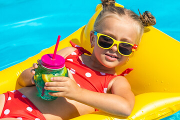 Cute little girl lying on inflatable mattress in swimming pool with blue water on warm summer day...