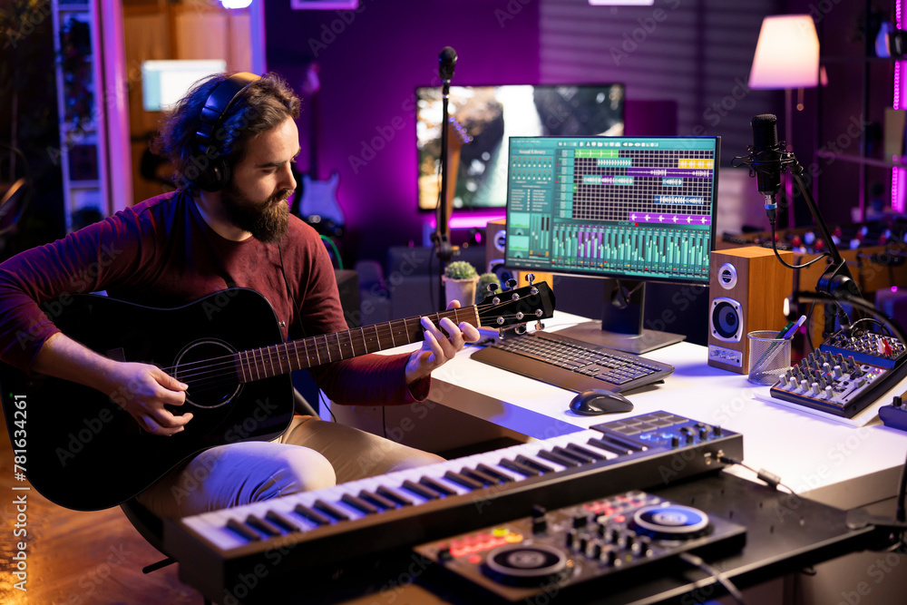 Poster young singer playing acoustic guitar and creating music with electronic tools in home studio, using 