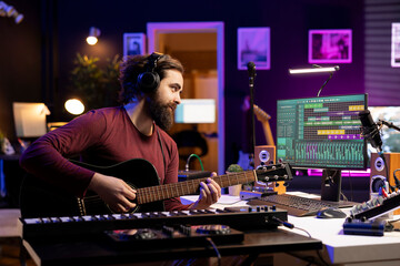 Music engineer playing new tunes on acoustic guitar and recording with daw software interface,...