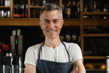 Closeup cropped portrait of mature handsome man cafe waiter standing near bar counter with arms...