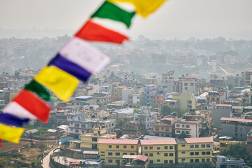View of Kathmandu with lot of low rise buildings through colorful prayer flags, hilltop view of...