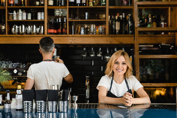 Middle-aged barista waiters restaurant staff brewing coffee in coffee machine, making drinks cocktails orders for customers in blue aprons at the bar counter