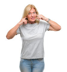 Middle age blonde woman over isolated background covering ears with fingers with annoyed expression for the noise of loud music. Deaf concept.