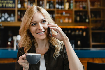 Beautiful caucasian woman talking on cellphone with colleagues, calling friends while drinking coffee for breakfast brunch in cafe restaurant