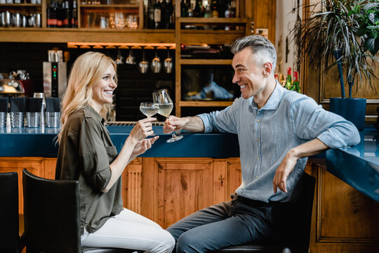 Love and relationship. Happy middle-aged couple drinking sparkling wine cocktails together on a romantic date toasting relaxing at the bar counter in cafe restaurant together. - Powered by Adobe