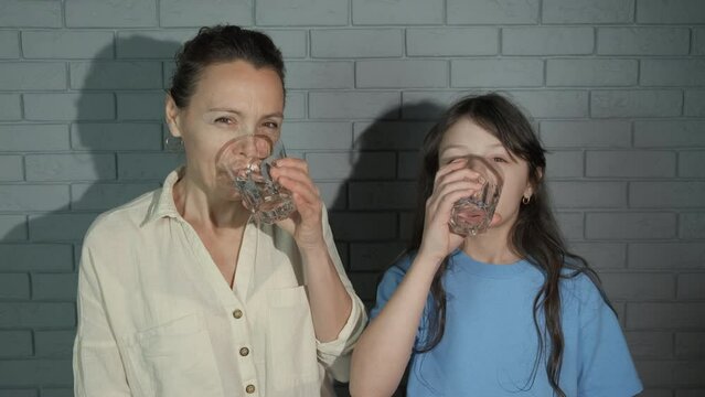 Family with healthy life water habit. A view of healthy mother with smiling child drink filtered water indoor.