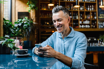 Caucasian mature middle-aged businessman boss freelancer relaxing in cafe restaurant drinking coffee and using cellphone for e-banking e-commerce, online shopping