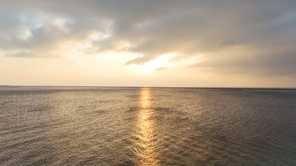 Sunset over calm sea with clouds partially covering the sun, casting a golden reflection on the water.