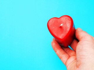 Red candle in heart shape in a hand over blue color background. Passion and romance concept. I give...