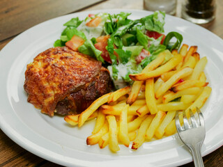 Burger with melted cheese toping, fresh green salad with lettuce and tomato and cucumber and fired potato chips on a wooden table. Tasty dinner. High quality product meal. Close up.