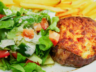 Burger with melted cheese toping, fresh green salad with lettuce and tomato and cucumber and fired potato chips on a wooden table. Tasty dinner. High quality product meal. Close up.