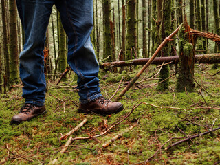 Tourist in blue jeans and tough brown leather outdoor boots on a green moss in a dense forest. Trip to nature and outdoor activity concept.