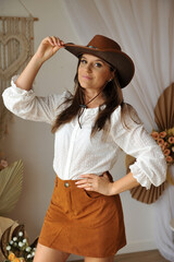 jovem mulher estilo vaqueira com bota cowtry, ambiente interior estilo boho tons marrons