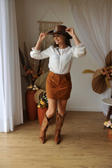 jovem mulher estilo vaqueira com bota cowtry, ambiente interior estilo boho tons marrons
