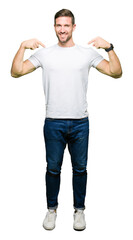 Handsome man wearing casual white t-shirt looking confident with smile on face, pointing oneself...