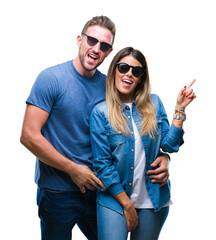 Young couple in love wearing sunglasses over isolated background with a big smile on face, pointing with hand and finger to the side looking at the camera.