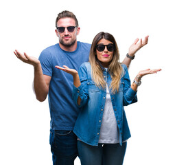 Young couple in love wearing sunglasses over isolated background clueless and confused expression...