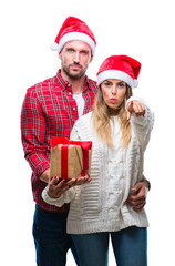 Young couple in love wearing christmas hat and holding present over isolated background pointing with finger to the camera and to you, hand sign, positive and confident gesture from the front