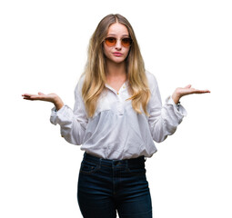 Young beautiful blonde woman wearing sunglasses over isolated background clueless and confused...