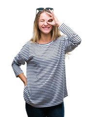 Young beautiful blonde woman wearing sunglasses over isolated background doing ok gesture with hand smiling, eye looking through fingers with happy face.