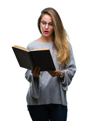 Young beautiful blonde woman reading a book over isolated background scared in shock with a surprise face, afraid and excited with fear expression