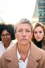 Fototapeta premium Vertical portrait a group of multiracial serious business women of diverse ages looking at the camera with serious and relaxed expression. A Caucasian woman with short hair standing in foreground