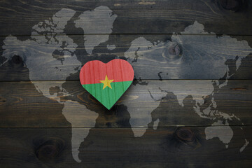 wooden heart with national flag of burkina faso near world map on the wooden background.