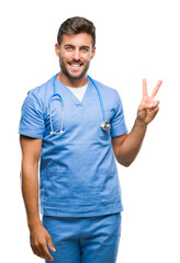 Young handsome doctor surgeon man over isolated background smiling with happy face winking at the camera doing victory sign. Number two.