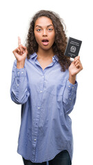 Obraz premium Young hispanic woman holding passport of Italy surprised with an idea or question pointing finger with happy face, number one