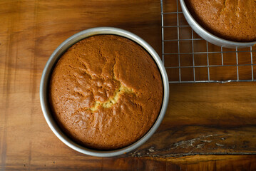 Freshly baked sponge cake cooling on wooden table.