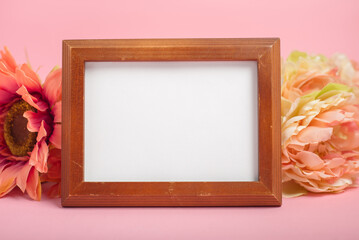 Wooden frame with white card and flowers on pink background. Mother's day card mockup.