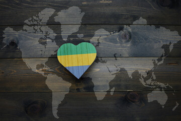 wooden heart with national flag of gabon near world map on the wooden background.