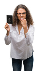 Fototapeta premium Young hispanic woman holding passport of United States of America annoyed and frustrated shouting with anger, crazy and yelling with raised hand, anger concept