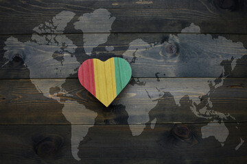 wooden heart with national flag of guinea near world map on the wooden background.