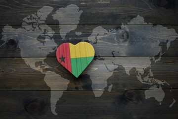 wooden heart with national flag of guinea bissau near world map on the wooden background.